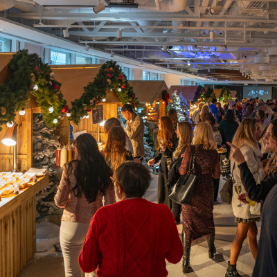 Guests explore festive wooden booths decorated with greenery and lights at an indoor holiday market in Washington, DC.